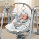 Happy newborn baby securely harnessed in plush seat of Ingenuity Swing ‘n Go Deluxe with toy bar overhead