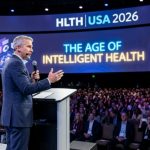 A keynote speaker addressing 12,000 healthcare leaders on the main stage at HLTH USA 2026 in Las Vegas with the event theme The Age of Intelligent Health displayed behind