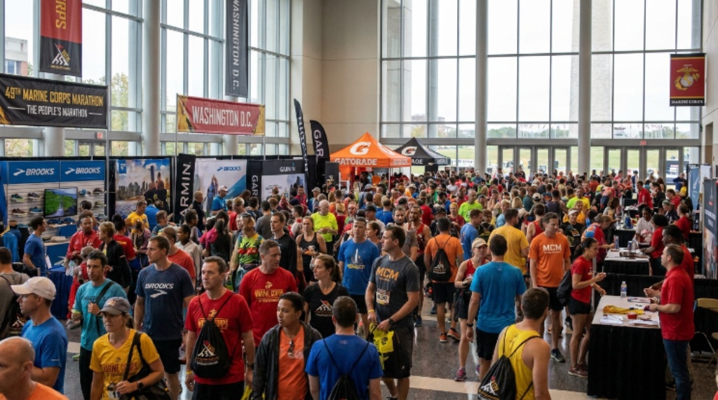 A crowd of fitness enthusiasts attending the Marine Corps Marathon Expo in Washington D.C., with vendor displays and banners visible in the background